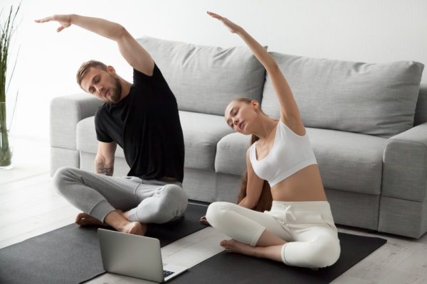 Couple doing yoga while seeking instruction from the laptop